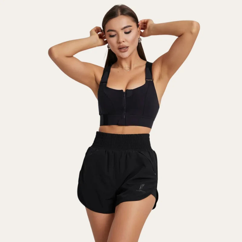 Modelo vestindo soutien desportivo Alba preto com fecho frontal de zíper, conjugado com calções desportivos pretos de cintura subida