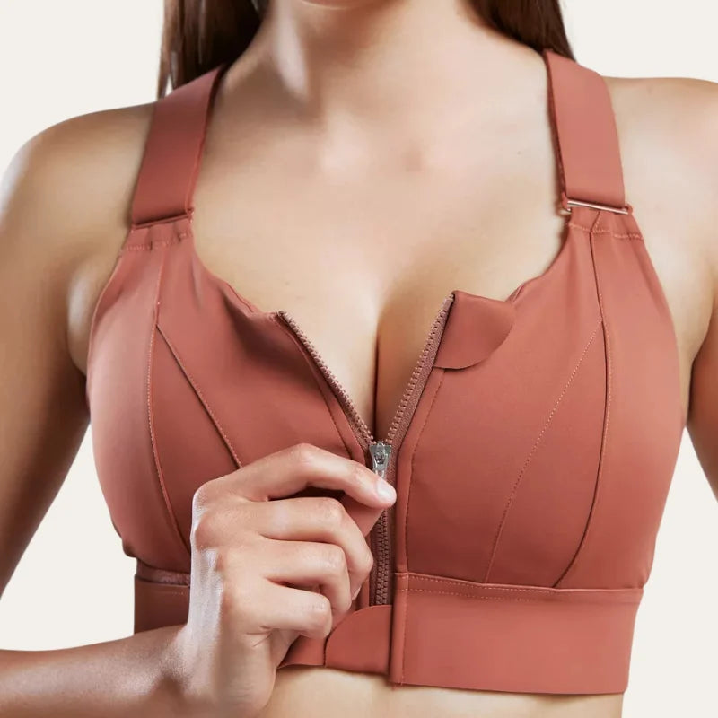 Mulher a fechar o fecho de correr do soutien desportivo Alba terracota, com cobertura alta e alças largas estruturadas