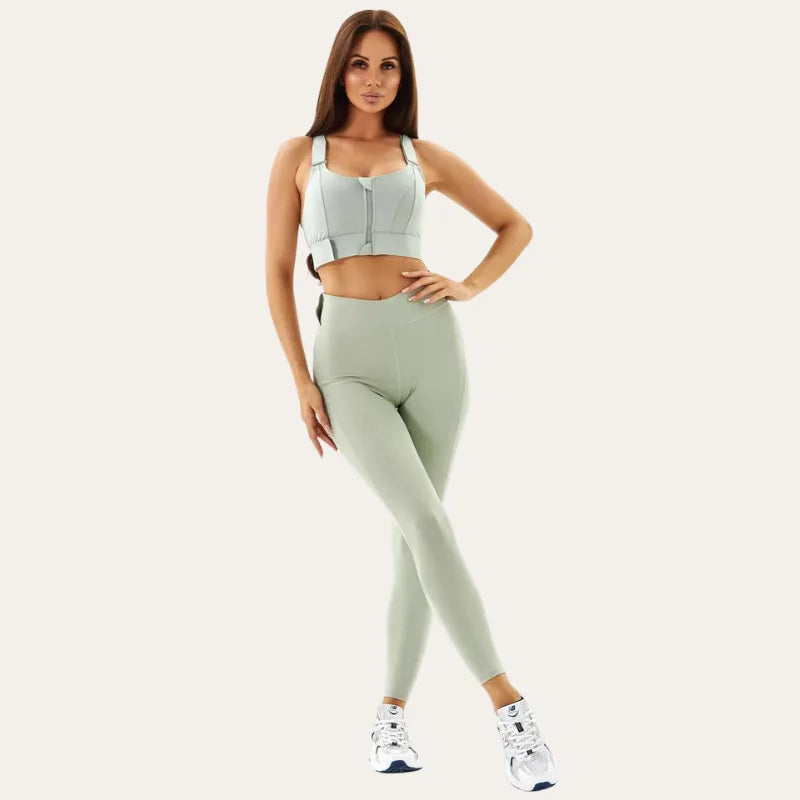 Modelo a usar o soutien desporti Alba verde acinzentado com leggings a condizer e ténis brancos, com a mão na cintura